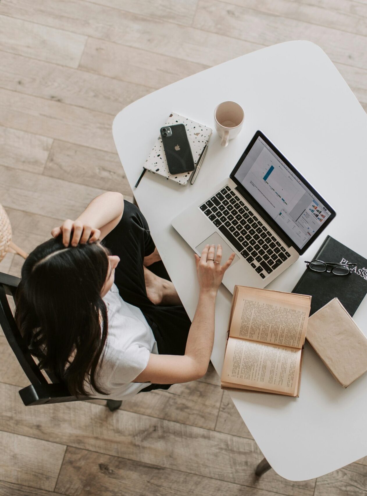 From above of young woman with long dark hair in casual clothes working at table and browsing netbook while sitting in modern workplace and touching hair